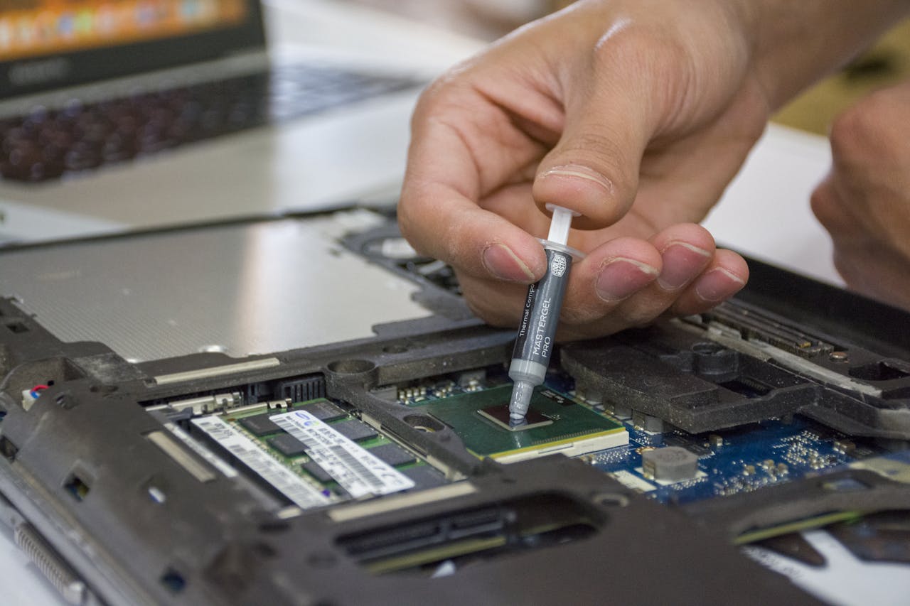 heros-img Close-up of hand applying thermal paste to a laptop microchip for maintenance.